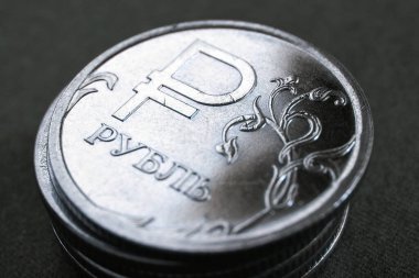 Parlak, parlayan Rus 1 1 ruble sikkesi. Üzerinde ulusal para biriminin resmi işareti var. Hem de çok karanlık ve neredeyse siyah bir arkaplanda. Rus ekonomisi hakkında çarpıcı bir illüstrasyon. Bozuk para maviye boyanmış.