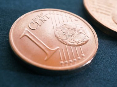Koyu mavi-gri bir yüzey üzerinde bir avro sent para yatıyor. Para yakın plan. Ekonomik ya da finansal tema üzerine illüstrasyon. Küçük paraların dolaşımdan çekilmesi ve fiyat etiketlerinin yuvarlanması. Makro