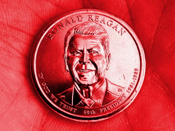 The American coin lies in the palm. 1 dollar coin with the portrait of President Ronald Reagan. Close-up. The illustration is tinted red. News about political system of the US. Republican Party. Macro