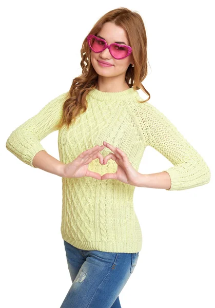 女孩在大粉红色眼镜使心形手势，穿着牛仔裤和绿色毛衣在工作室在白色背景摆姿势 — 图库照片