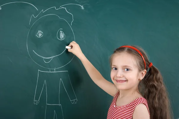 Colegiala niño en vestido de rayas rojas dibujo hombre feliz en el fondo de pizarra verde, concepto de vacaciones de la escuela de verano —  Fotos de Stock