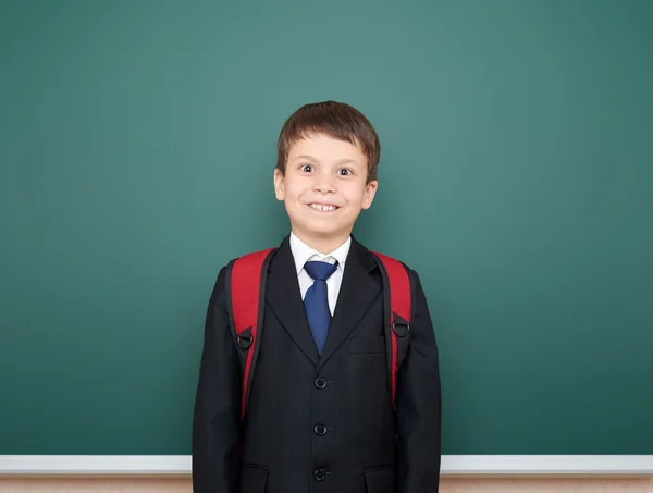 School boy portrait in black suit on green chalkboard background with red backpack, education concept — Stock Photo, Image