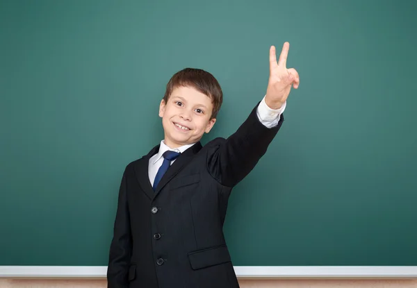 Menino da escola em terno preto mostrar gesto de dois dedos no fundo quadro verde, conceito de educação — Fotografia de Stock