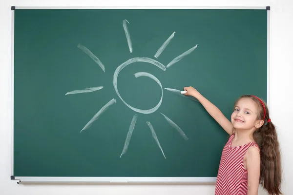 Schoolmeisje kind in rood gestreepte jurk tekening zon op groene schoolbord achtergrond, zomer school vakantie concept — Stockfoto