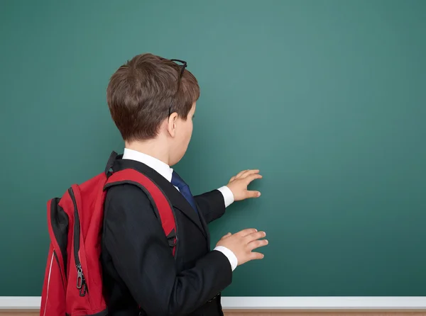 School jongen portret in zwart pak op groene schoolbord achtergrond met rode rugzak, onderwijsconcept — Stockfoto