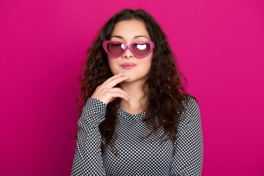 genç kadın güzel portre, poz pembe bir arka plan, uzun kıvırcık saç, kalp şeklinde, glamour kavramı güneş gözlüğü