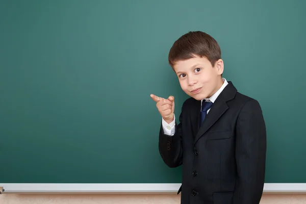 Menino da escola em terno preto mostrar gesto dedo, no fundo quadro verde, conceito de educação — Fotografia de Stock