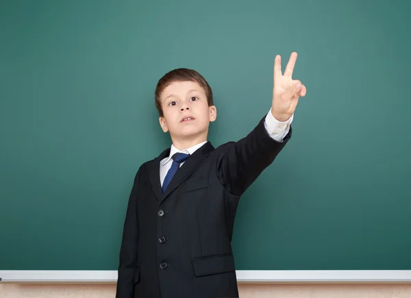 Menino da escola em terno preto mostrar gesto de dois dedos no fundo quadro verde, conceito de educação — Fotografia de Stock