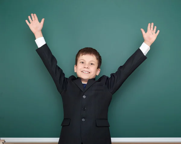 School jongen in zwart pak open armen op groene schoolbord achtergrond, onderwijsconcept — Stockfoto