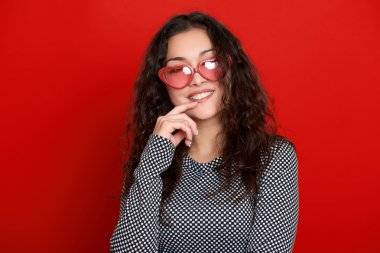 genç kadın güzel portre, poz kırmızı arka plan, uzun kıvırcık saç, kalp şeklinde, glamour kavramı güneş gözlüğü