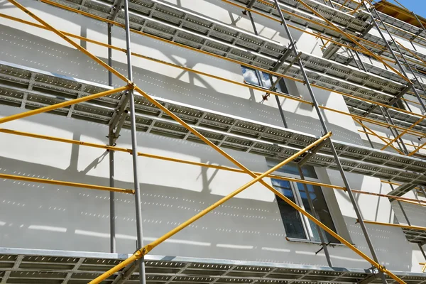 Gerüst in der Nähe eines im Bau befindlichen Hauses für Außenputzarbeiten, hohes Wohnhaus in der Stadt, weiße Wand und Fenster, gelbes Rohr — Stockfoto