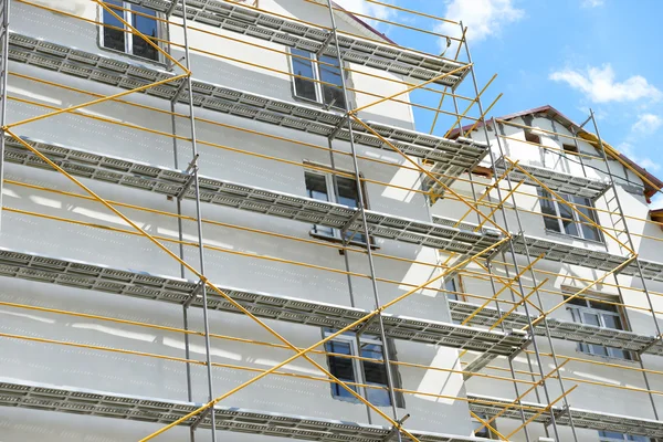 Andamios cerca de una casa en construcción para trabajos externos de yeso, edificio de apartamentos altos en la ciudad, pared blanca y ventana, tubería amarilla — Foto de Stock