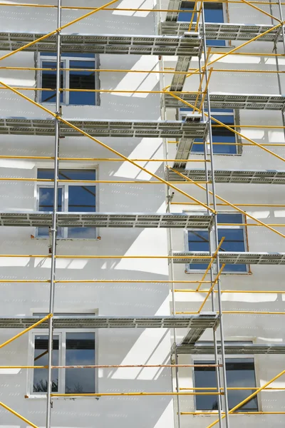 Andaimes perto de uma casa em construção para obras de gesso externo, prédio de apartamentos altos na cidade, parede branca e janela, tubo amarelo — Fotografia de Stock