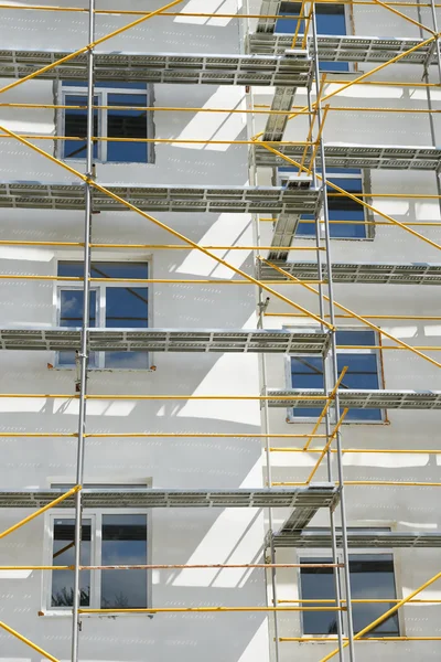 Gerüst in der Nähe eines im Bau befindlichen Hauses für Außenputzarbeiten, hohes Wohnhaus in der Stadt, weiße Wand und Fenster, gelbes Rohr — Stockfoto