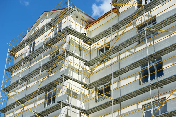 Gerüst in der Nähe eines im Bau befindlichen Hauses für Außenputzarbeiten, hohes Wohnhaus in der Stadt, weiße Wand und Fenster, gelbes Rohr — Stockfoto
