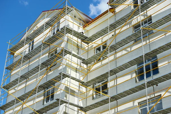 Ponteggi vicino a una casa in costruzione per lavori di intonaco esterno, edificio alto appartamento in città, parete bianca e finestra, tubo giallo — Foto Stock