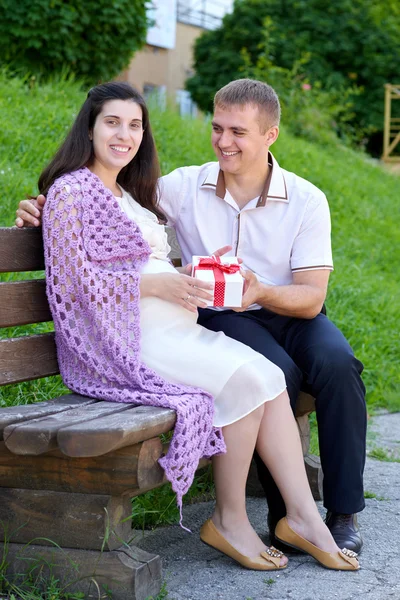 Schwangere nimmt Geschenk von ihrem Mann, glückliche Familie, Paar im Stadtpark, Sommersaison, grünes Gras und Bäume — Stockfoto