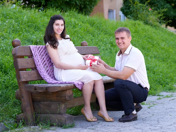 Terhes nő vesz egy ajándék a férje, boldog család, pár, a városi park, a nyári szezonban, a zöld fű és a fák — Stock Fotó