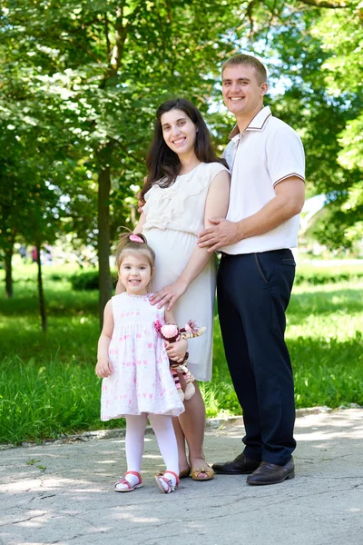 Familienporträt im sommerlichen Stadtpark, schwangere Frau mit Kind und Mann, grünes Gras und Bäume — Stockfoto