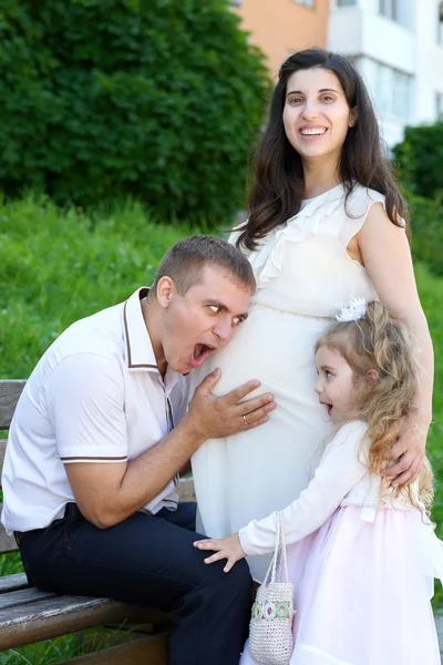 Muž a dítě poslouchat břicho těhotná žena, šťastná rodina, pár v městském parku, letní sezóny, zelené trávy a stromů — Stock fotografie