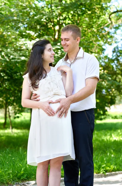 Mulher grávida com marido posando no parque da cidade, retrato de família, temporada de verão, grama verde e árvores — Fotografia de Stock