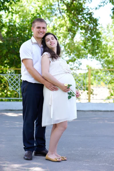 Mulher grávida com marido posando no parque da cidade, retrato de família, temporada de verão, grama verde e árvores — Fotografia de Stock