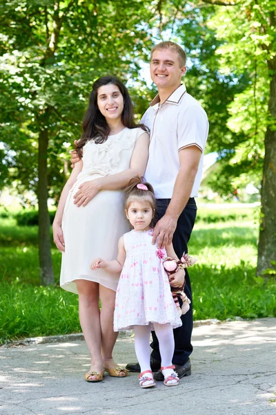 Mulher grávida com marido posando no parque da cidade, retrato de família, temporada de verão, grama verde e árvores — Fotografia de Stock