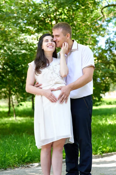 Těhotná žena s manželem pózuje v městském parku, rodinný portrét, letní sezóny, zelené trávy a stromů — Stock fotografie
