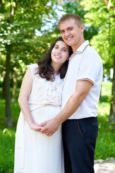 Zwangere vrouw met echtgenoot poseren in het stadspark, familieportret, zomerseizoen, groen gras en bomen — Stockfoto