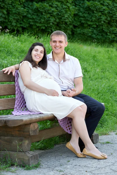 Gravid kvinna och man på utomhus, lycklig familj, par i stadsparken, sommarsäsongen, grönt gräs och träd — Stockfoto