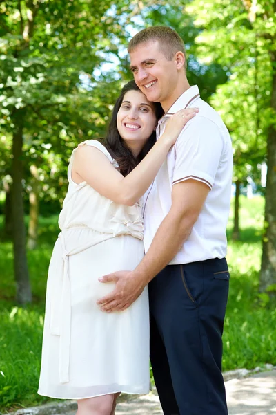 Zwangere vrouw met echtgenoot poseren in het stadspark, familieportret, zomerseizoen, groen gras en bomen — Stockfoto