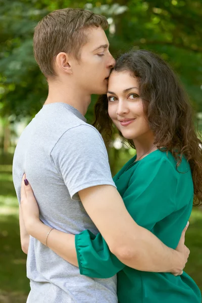 Романтическая пара позирует в городском парке, летний сезон, молодежь сзади — стоковое фото
