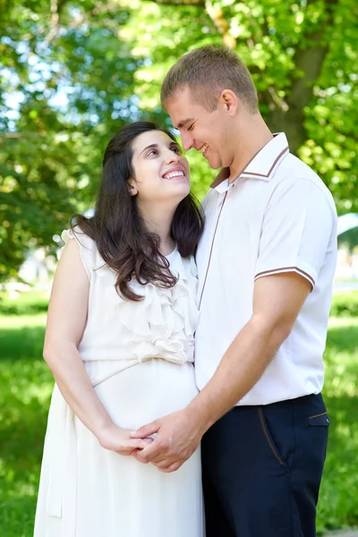 Zwangere vrouw met echtgenoot poseren in het stadspark, familieportret, zomerseizoen, groen gras en bomen — Stockfoto