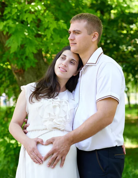 Terhes nő férje pózol a városi park, a családi portré, a nyári szezonban, a zöld fű és a fák — Stock Fotó