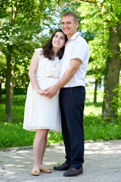 Gravid kvinna med man poserar i stadsparken, familjeporträtt, sommarsäsongen, grönt gräs och träd — Stockfoto