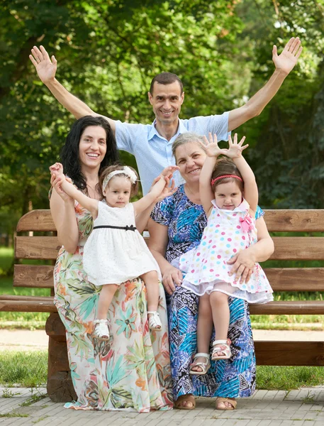 Família grande senta-se no banco de madeira no parque da cidade e acenando, estação de verão, criança, pai e avó, grupo de cinco pessoas — Fotografia de Stock