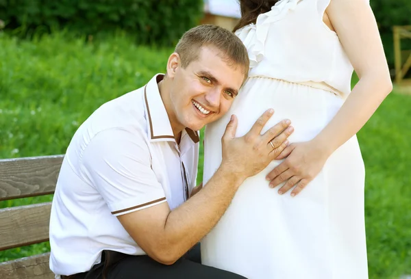 pregnant woman and husband, man listen belly and talk with baby,