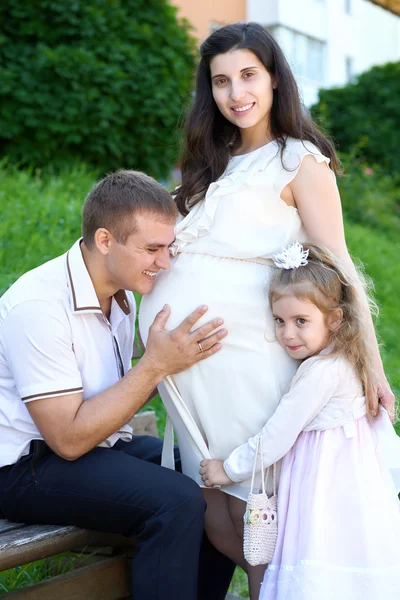 Homem e criança ouvir barriga de mulher grávida, família feliz, casal no parque da cidade, temporada de verão, grama verde e árvores — Fotografia de Stock