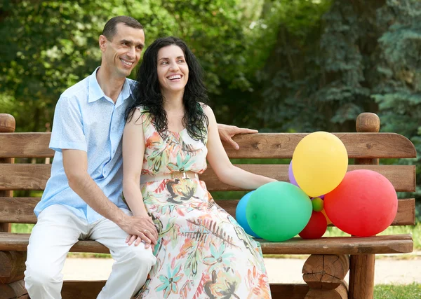 Boldog romantikus pár léggömb ülni a padon, a Városliget és jelentő, a nyári szezonban, felnőtt emberek férfi és nő — Stock Fotó