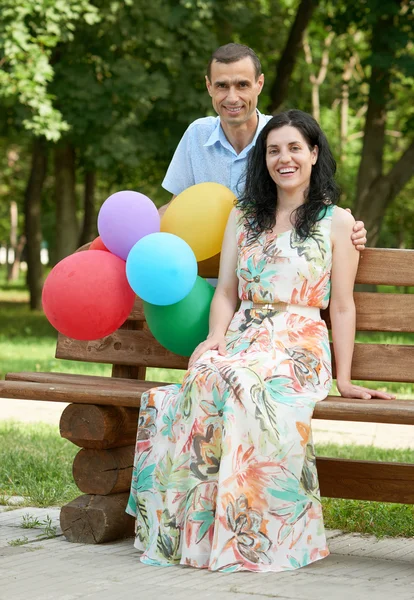 幸福浪漫的情侣与气球坐在长凳上的城市公园和构成、 夏季、 成人人男人和女人 — 图库照片