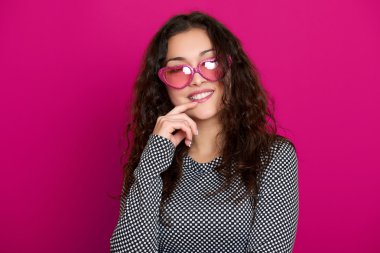 genç kadın güzel portre, poz pembe bir arka plan, uzun kıvırcık saç, kalp şeklinde, glamour kavramı güneş gözlüğü