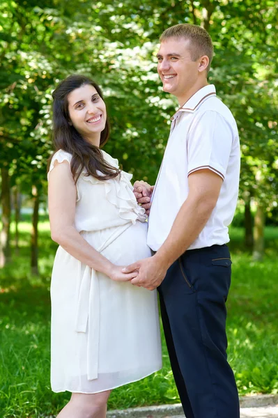 Mulher grávida com marido posando no parque da cidade, retrato de família, temporada de verão, grama verde e árvores — Fotografia de Stock