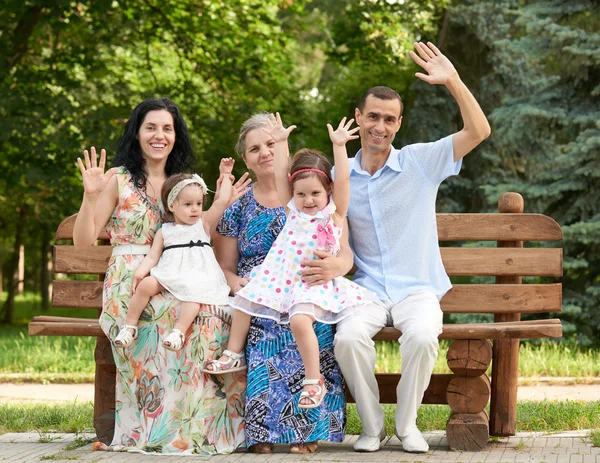 Große Familie sitzt auf Holzbank im Stadtpark und winkt, Sommersaison, Kind, Eltern und Großmutter, Gruppe von fünf Personen — Stockfoto