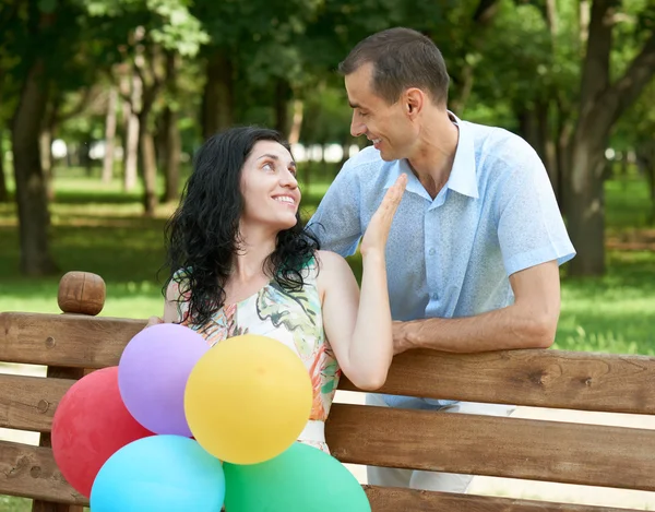 Щаслива романтична пара з повітряною кулею сидить на лавці в міському парку і позує, літній сезон, дорослі люди чоловік і жінка — стокове фото