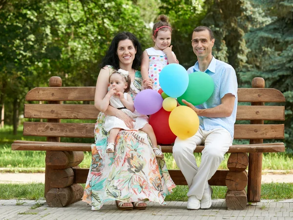 Happy family sit on wooden bench in city park, summer season, child and parent , group of four people — Stock Photo, Image