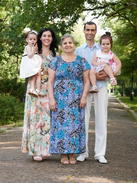 Family portrait in summer city park, parents with child and grandmother, summer season, green grass and trees — Stock Photo, Image