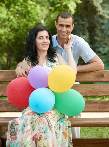 Šťastný romantický pár s balónem sedět na lavici v městském parku a pózování, letní sezóny, dospělých lidí muž a žena — Stock fotografie