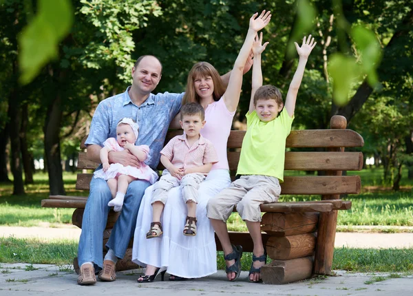 Portrait de famille heureux en plein air, groupe de cinq personnes assis sur un banc en bois dans le parc de la ville, saison estivale, enfant et parent — Photo