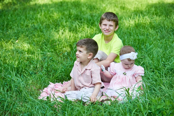 Tre barn sitta i gräset, spela och ha roligt. — Stockfoto