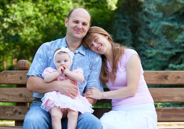 快乐家庭肖像与女婴在室外，坐在木凳上在城市公园，夏天的季节，孩子和家长 — 图库照片
